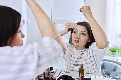 Middle aged woman treating her hair using medical drops. Stock Photo