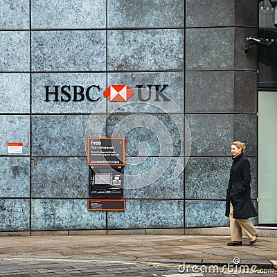 Middle aged woman walks past an Automatic Teller Machine from the HSBC bank advertising free cash withdrawals Editorial Stock Photo