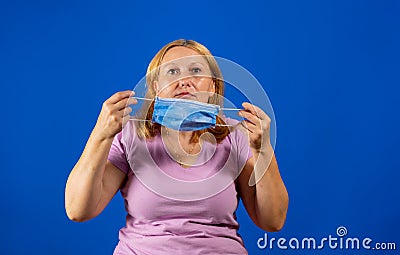 Middle blonde woman taking off her medical mask isolated on blue background Stock Photo