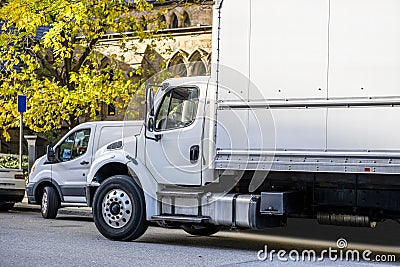 Middle class day cab rig semi truck with box trailer and cargo mini van make deliveries to customers standing on the city street Editorial Stock Photo
