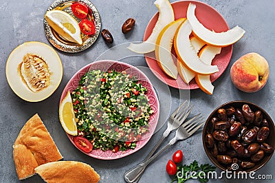 Middle Eastern and Arab food tabbouleh salad, pita, melon, peach and dates on a gray background. Top view, flat lay Stock Photo