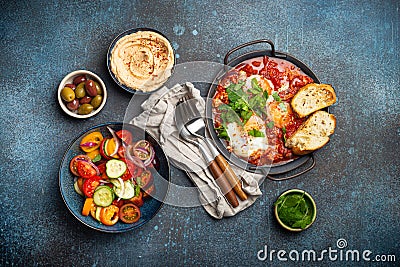 Middle Eastern breakfast or brunch with Shakshouka in pan, toasts, vegetables salad, hummus, olives Stock Photo