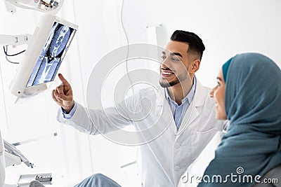 Middle-Eastern Stomatologist Showing Teeth Xray Picture On Digital Monitor To Islamic Female Stock Photo