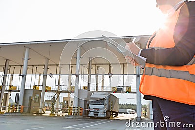 Midsection of female worker writing on clipboard while looking at truck entering in shipping yard Stock Photo