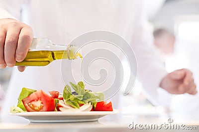 Midsection of mature chef using pouring oil on salad in plate at restaurant Stock Photo