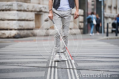 Midsection of young blind man with white cane walking across the street in city. Stock Photo