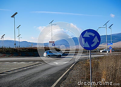 Roundabout traffic sign, passing cars in the background, solar panels providing the light at night. Editorial Stock Photo