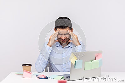 Migraine of stressful job. Depressed man employee sitting in office, clasping head temples, suffering headache Stock Photo