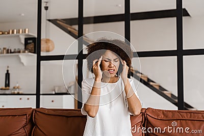 Migraine is a strong headache of african american woman. Overstressed woman touches her head because of pain. Depression Stock Photo