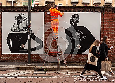 Workers are putting up posters showcasing the Moncler collection of 2023 on the walls, Milan Editorial Stock Photo