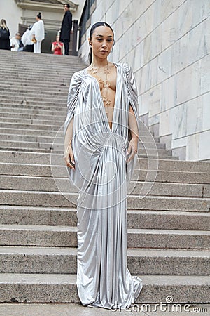 Woman with long silver dress with plunging neckline and golden necklace before Genny fashion Editorial Stock Photo