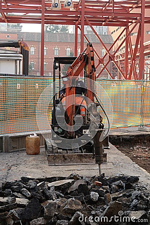 Demolition of the asphalt of a road with a jackhammer. Small excavator with demolition hammer. In the background steel trellis Editorial Stock Photo