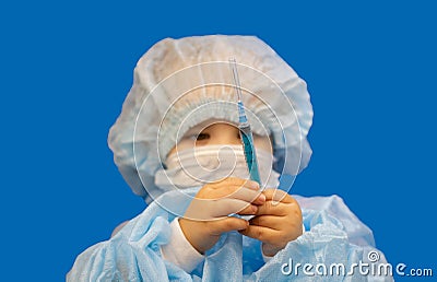 Mile doctor girl holds a syringe in front of her on a blue background. The child carefully measures the dose of medicine Stock Photo