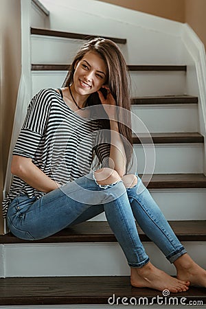 Miling Caucasian young beautiful woman model with messy long hair in ripped blue jeans and striped t-shirt Stock Photo