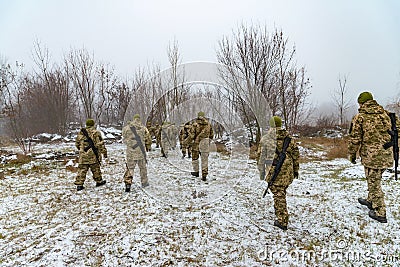 The military in camouflage with Kalashnikov assault rifles, behind their backs, go forward to attack the enemy in winter Stock Photo