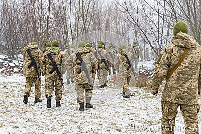 The military in camouflage with Kalashnikov assault rifles, behind their backs, go forward to attack the enemy in winter Editorial Stock Photo