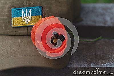 Ukraine. 06/13/2020. A military cap with the flag of Ukraine lies on a wooden table, on a hat a red poppy flower. Editorial Stock Photo