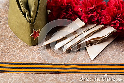military cap with old letters, a St. George ribbon and carnations, against a texture background with an inscription Stock Photo