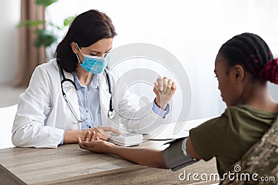 Military Healthcare. Doctor Wearing Medical Mask Measuring Blood Pressure For Soldier Woman Stock Photo