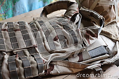 A military helmet of a Ukrainian soldier with a heavy bulletproof vest on wooden table in checkpoint dugout Stock Photo