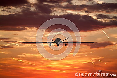 military UAV airplane flies against backdrop of beautiful sunset sky is orange with clouds and condensation traces Stock Photo