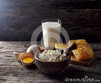 Milk in glass, honeycomb and eggs on a wooden background. Cottage cheese in a wooden bowl, rustic style. Dairy products in the mo Stock Photo