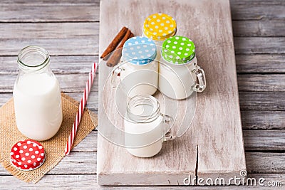 Milk jars with colorful caps on a cutting board, cinnamon and drinking straw Stock Photo