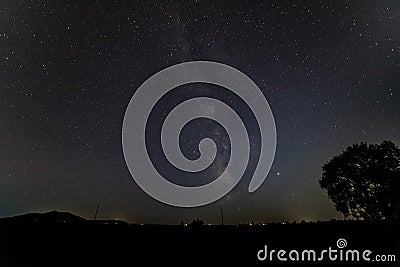 The Milky way over a black silhouette horizon with a tree Stock Photo