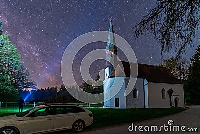 The milkyway with its galactical centre as background of a church at night while a man enlightens the night sky with his Stock Photo