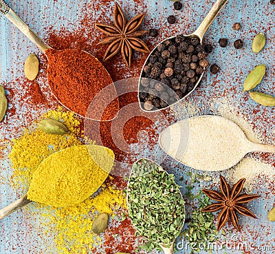 Milled spices - garlic, turmeric, paprika, anise, oregano, cardamom. Round of golden spoons on blue wooden table. Top Stock Photo