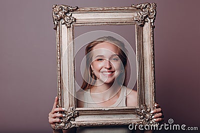 Millenial young woman blonde hair holds gilded picture frame in hands face portrait Stock Photo