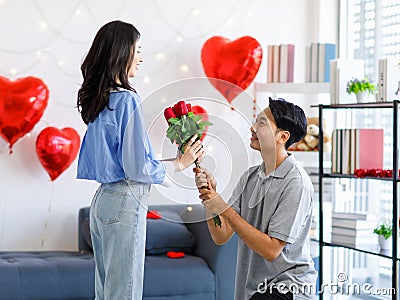 Millennial Asian young romantic lover couple male boyfriend kneel down giving red roses bouquet surprising female girlfriend Stock Photo