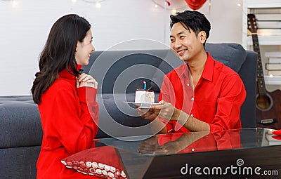 Millennial Asian young romantic lover couple male boyfriend in red outfit sitting on floor giving surprising female girlfriend Stock Photo