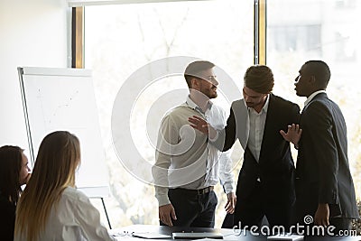 Millennial businessman setting apart two aggressive multiracial coworkers. Stock Photo