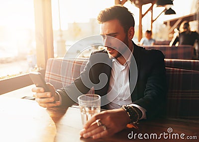 Millennial businessman sitting in a cafe at a table and looking at the screen of his mobile phone. Stock Photo