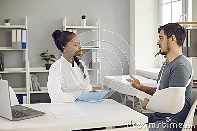 Millennial caucasian man patient with broken hand talk to afro american doctor Stock Photo