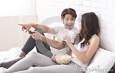 Millennial couple watching movie with popcorn, sitting in bed Stock Photo