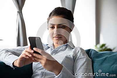 Millennial ethnic woman rest on couch using cellphone Stock Photo