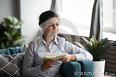 Millennial ethnic woman distracted from reading dreaming Stock Photo