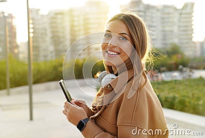 Millennial. Portrait female. Teens looking at camera. Mobile app. Headset phone. Smartwatch. Sunlights rays. Sunset. Winter Stock Photo