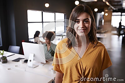 Millennial white female creative standing in a busy casual office, smiling to camera Stock Photo