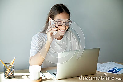 Millennial woman in glasses talking on mobile and using laptop Stock Photo