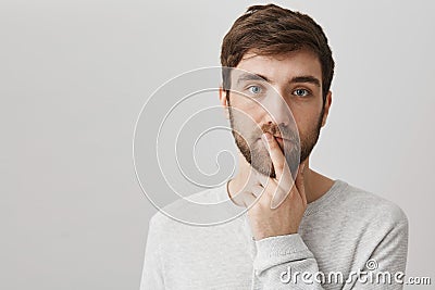 Mindful and calm good-looking male with beard holding index finger over mouth and standing over gray background Stock Photo