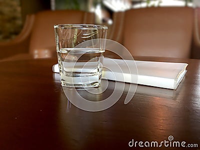 Mineral drink water in transparent glass with notebook on brown wooden table. Stock Photo