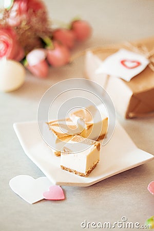 Mini cheese cake platter - caramel cheese cake on white plate with pink peomies and brown paper wrapped present Stock Photo