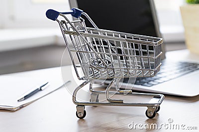 Mini empty shop cart trolley over a laptop computer on wood table background Stock Photo