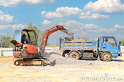 Mini excuvator loading gravel to dumper truck Stock Photo