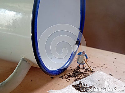 Photo Mini figure toy woman cleaning spilled tea at wooden board beyond small white aluminium glass Stock Photo