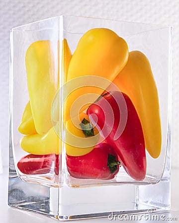 Mini fresh multicolored peppers, stacked in a rectangular glass vase Stock Photo