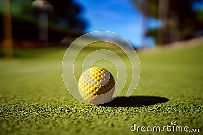 Mini Golf yellow ball on green grass at sunset Stock Photo